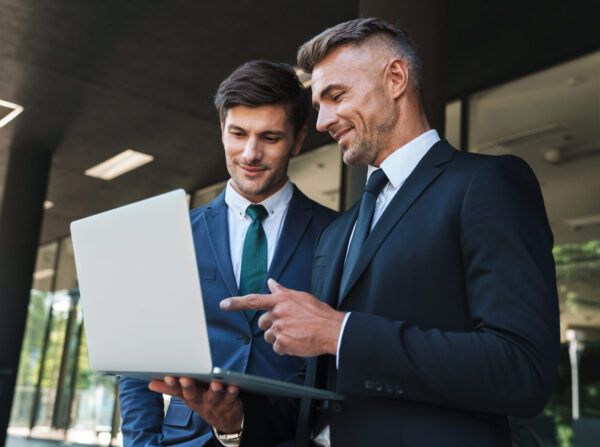 Portrait Of Caucasian Businessmen Partners Standing Outside Office Center And Using Laptop Together During Working Meeting