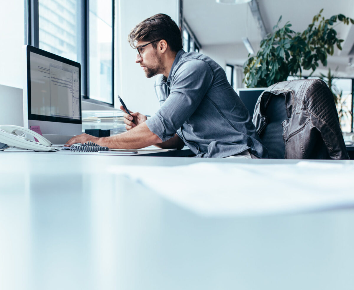 Young,man,sitting,in,office,and,working,on,desktop,pc.